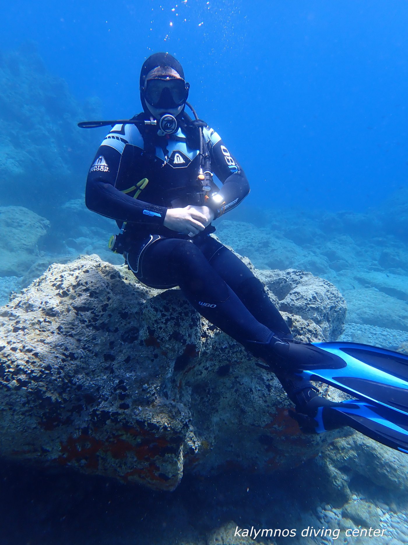 A scuba diver resting on a rock in clear blue Aegean water